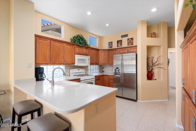 kitchen with white appliances, a breakfast bar, backsplash, sink, and kitchen peninsula