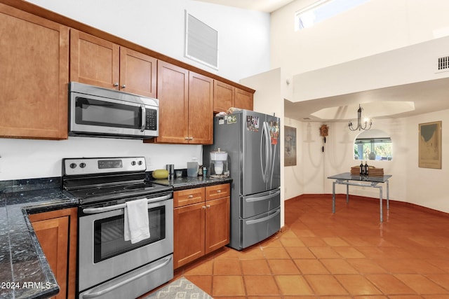 kitchen featuring dark stone countertops, a towering ceiling, appliances with stainless steel finishes, and light tile patterned flooring