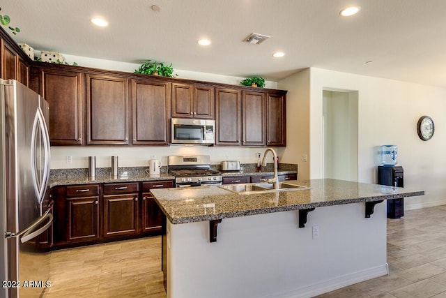 kitchen featuring a breakfast bar, sink, appliances with stainless steel finishes, an island with sink, and dark stone counters