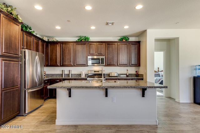 kitchen featuring light stone countertops, appliances with stainless steel finishes, a kitchen island with sink, and a breakfast bar area