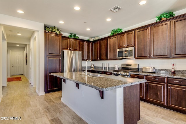 kitchen with sink, a breakfast bar area, light hardwood / wood-style flooring, appliances with stainless steel finishes, and a kitchen island with sink