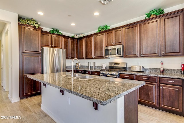 kitchen with a breakfast bar, sink, a kitchen island with sink, stainless steel appliances, and light stone countertops