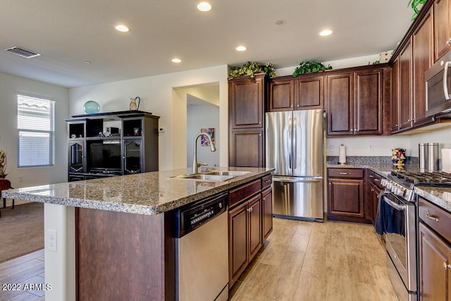 kitchen featuring stainless steel appliances, sink, light stone countertops, and an island with sink