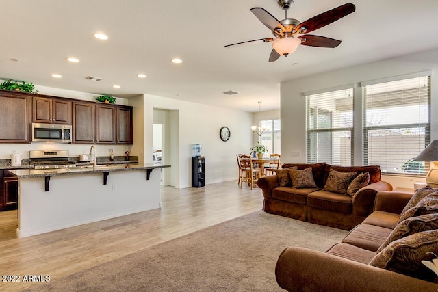 living room with sink, ceiling fan with notable chandelier, and light wood-type flooring