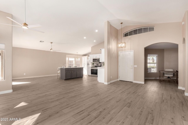 unfurnished living room featuring high vaulted ceiling, ceiling fan with notable chandelier, wood finished floors, visible vents, and baseboards