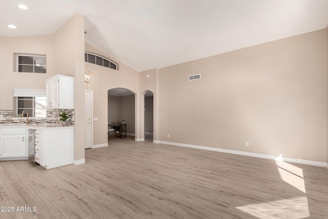 unfurnished living room with light wood-type flooring, sink, and high vaulted ceiling