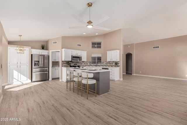 kitchen featuring decorative backsplash, appliances with stainless steel finishes, a kitchen island, ceiling fan, and white cabinetry