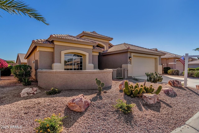 mediterranean / spanish-style home featuring a fenced front yard, a garage, a tile roof, driveway, and stucco siding