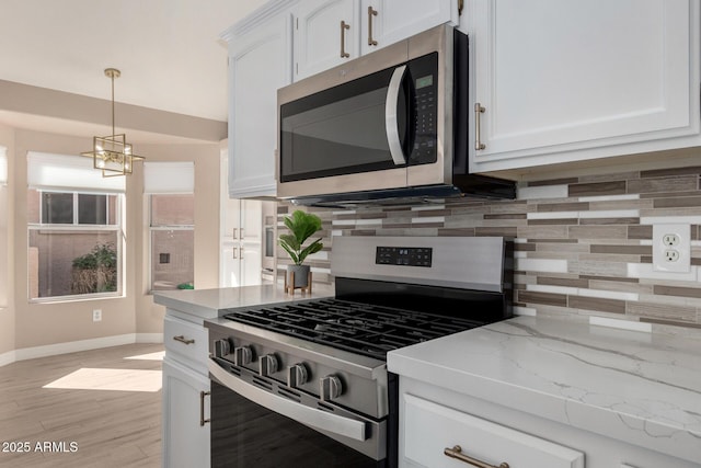 kitchen with white cabinets, hanging light fixtures, appliances with stainless steel finishes, decorative backsplash, and light wood finished floors