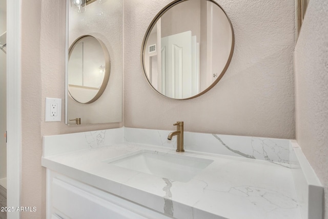 bathroom featuring visible vents, a textured wall, and vanity