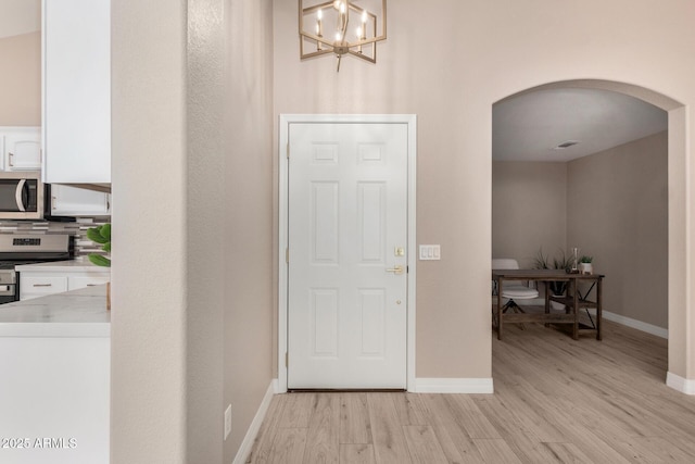 foyer featuring arched walkways, light wood-style flooring, and baseboards