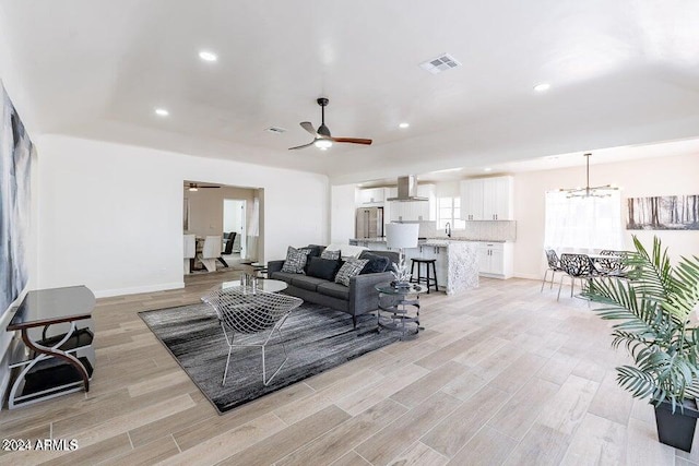 living room with ceiling fan with notable chandelier, light wood-type flooring, and sink