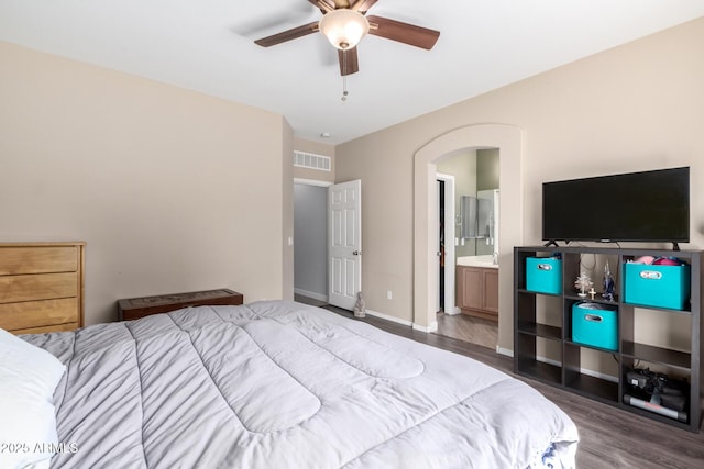 bedroom with wood finished floors, visible vents, baseboards, ensuite bath, and arched walkways