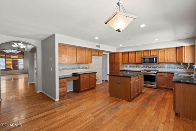 2024 N 125th Ave, Avondale, AZ 85392 - kitchen featuring appliances with stainless steel finishes, brown cabinets, arched walkways, decorative backsplash, and wood-type flooring