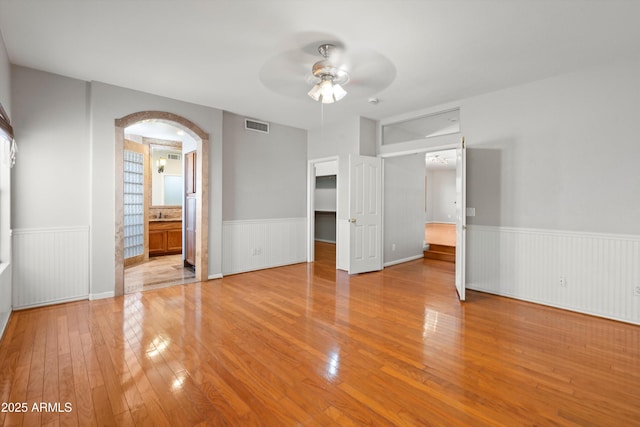 2024 N 125th Ave, Avondale, AZ 85392 - unfurnished bedroom featuring a wainscoted wall, light wood finished floors, arched walkways, a spacious closet, and ensuite bath