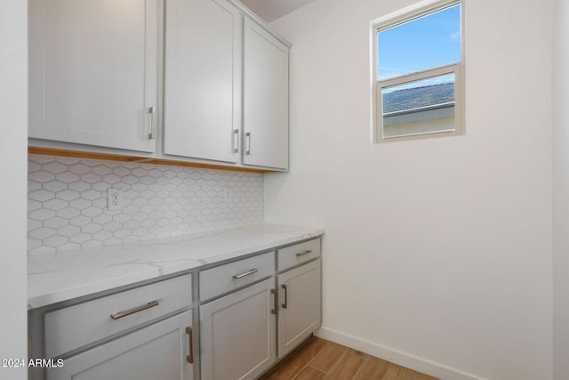 interior space with tasteful backsplash, light stone countertops, and light wood-type flooring