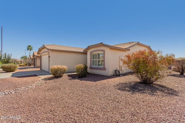 view of side of property featuring stucco siding, a garage, concrete driveway, and a tiled roof