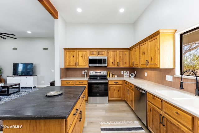 kitchen featuring sink, ceiling fan, light wood-type flooring, appliances with stainless steel finishes, and a kitchen island