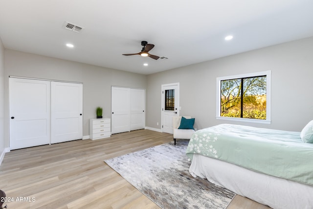 bedroom featuring ceiling fan, light hardwood / wood-style floors, and multiple closets