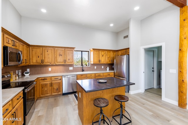 kitchen featuring a breakfast bar, light hardwood / wood-style flooring, a towering ceiling, appliances with stainless steel finishes, and a kitchen island