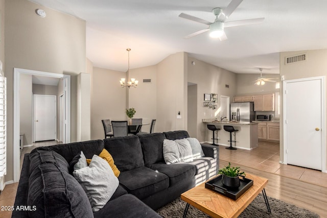 living room with ceiling fan with notable chandelier, high vaulted ceiling, and light hardwood / wood-style flooring