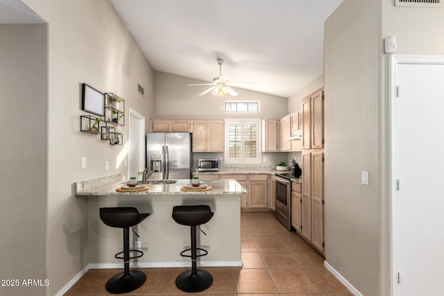 kitchen with light brown cabinetry, a breakfast bar, stainless steel appliances, vaulted ceiling, and tile patterned flooring