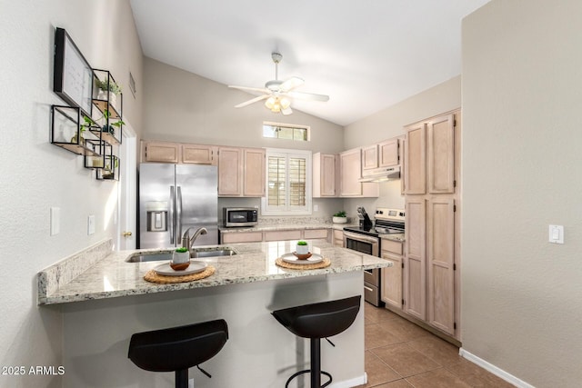 kitchen featuring a kitchen bar, light tile patterned floors, light brown cabinetry, and appliances with stainless steel finishes