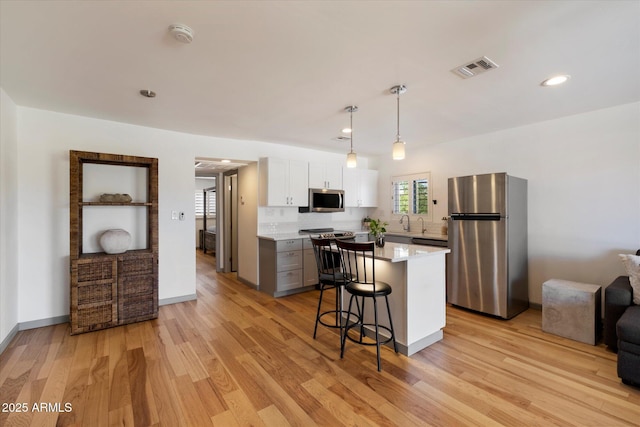 7430 E Chaparral Rd Unit A222, Scottsdale, AZ 85250 - kitchen featuring stainless steel appliances, a center island, light wood finished floors, a kitchen bar, and decorative light fixtures