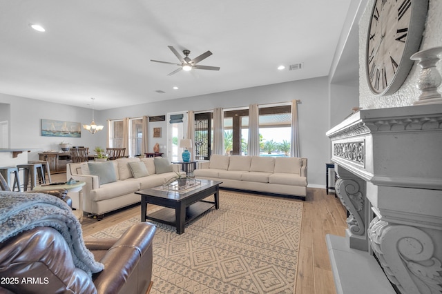 living room with ceiling fan with notable chandelier and light hardwood / wood-style floors