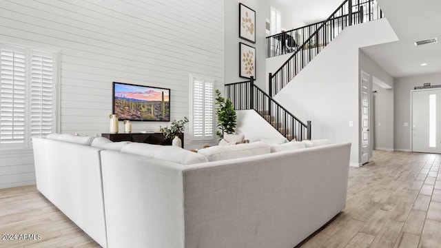 living room featuring visible vents, wood walls, stairway, light wood-type flooring, and a high ceiling