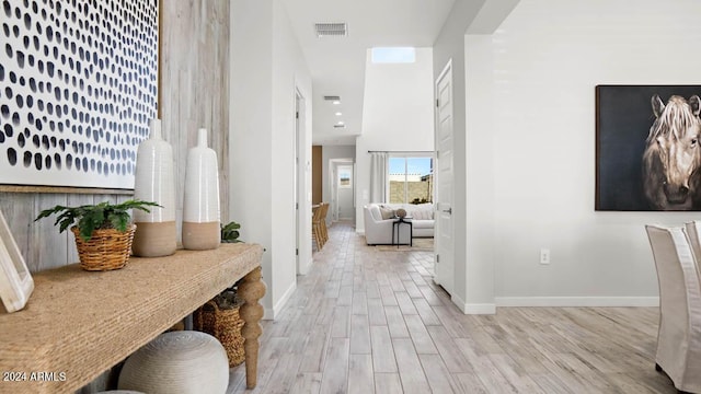 hall featuring a towering ceiling, baseboards, visible vents, and wood finished floors