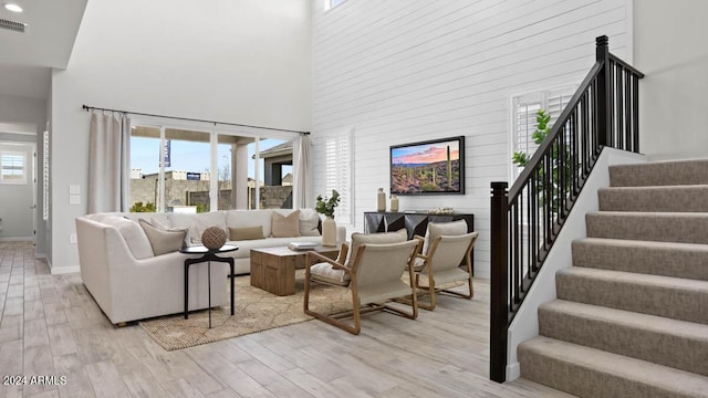 living room featuring light wood-style flooring, baseboards, visible vents, stairway, and a high ceiling