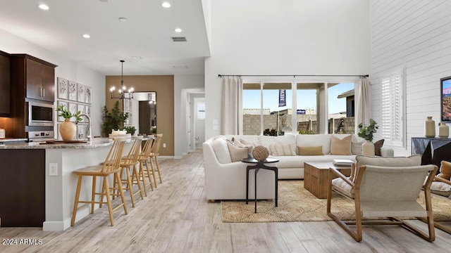 living area with an inviting chandelier, a high ceiling, light wood-type flooring, and recessed lighting