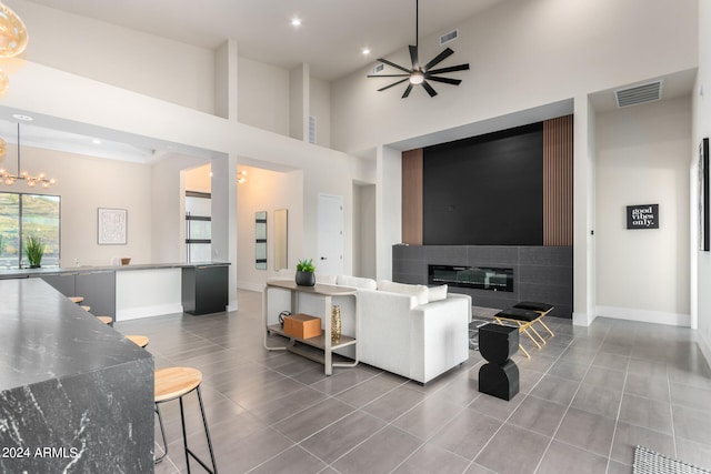 living room featuring a high ceiling, ceiling fan with notable chandelier, and a tile fireplace