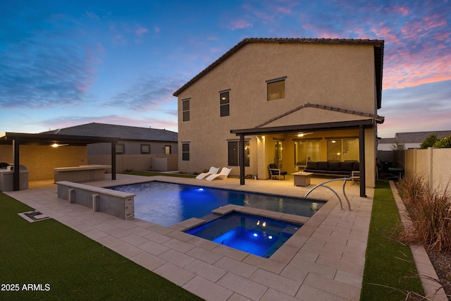 pool at dusk featuring a fenced backyard, an outdoor hangout area, an in ground hot tub, exterior kitchen, and a patio area