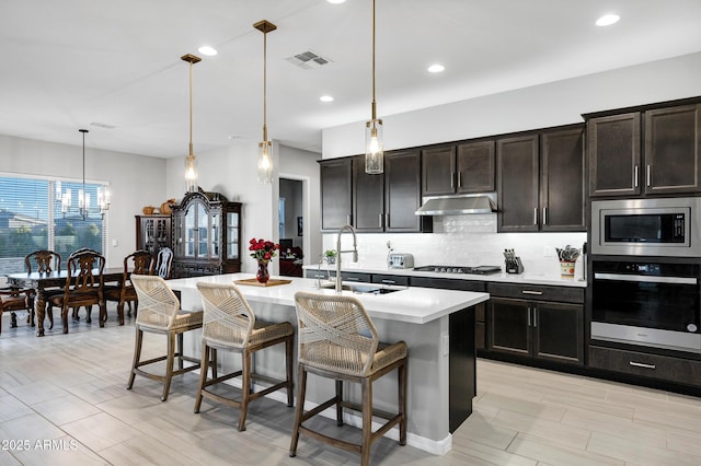 kitchen featuring tasteful backsplash, visible vents, appliances with stainless steel finishes, under cabinet range hood, and a sink