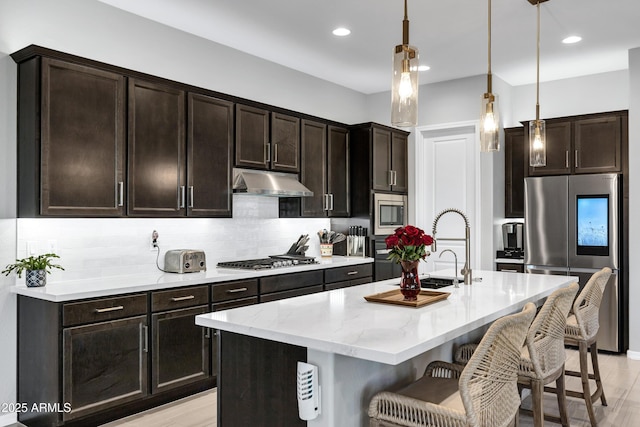 kitchen featuring stainless steel appliances, tasteful backsplash, a sink, under cabinet range hood, and a kitchen breakfast bar