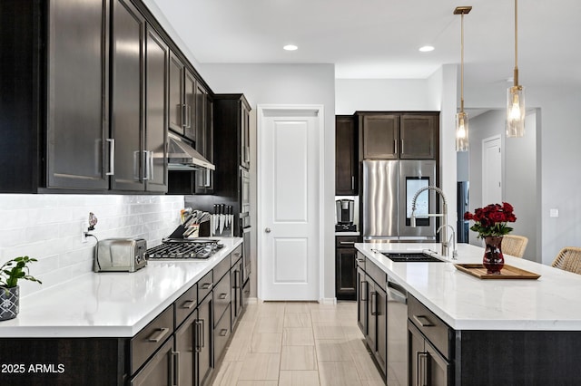 kitchen with under cabinet range hood, stainless steel appliances, backsplash, an island with sink, and pendant lighting