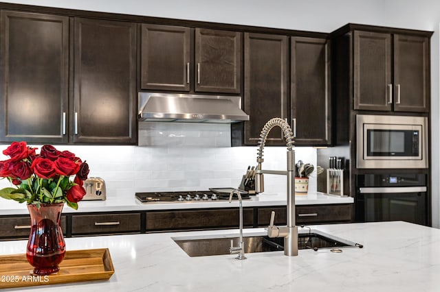 kitchen with oven, under cabinet range hood, a sink, backsplash, and stainless steel microwave