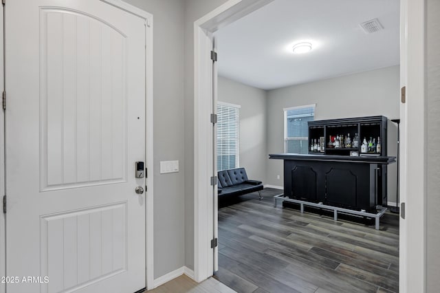 foyer featuring a bar, wood finished floors, visible vents, and baseboards