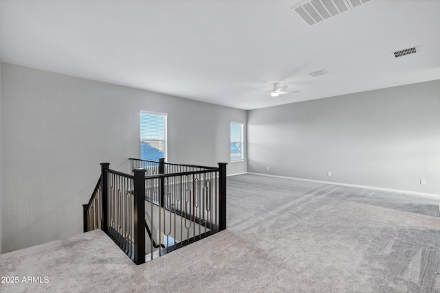 carpeted spare room with visible vents, a ceiling fan, and baseboards