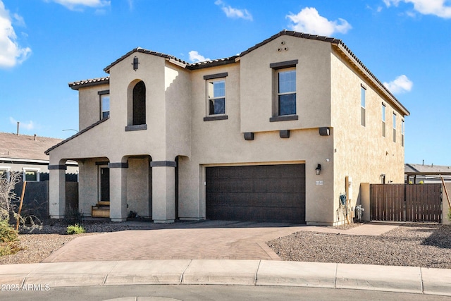 mediterranean / spanish-style house featuring decorative driveway, a tile roof, stucco siding, an attached garage, and a gate