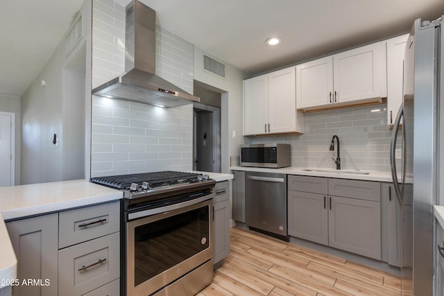 kitchen featuring a sink, appliances with stainless steel finishes, gray cabinetry, wall chimney range hood, and visible vents