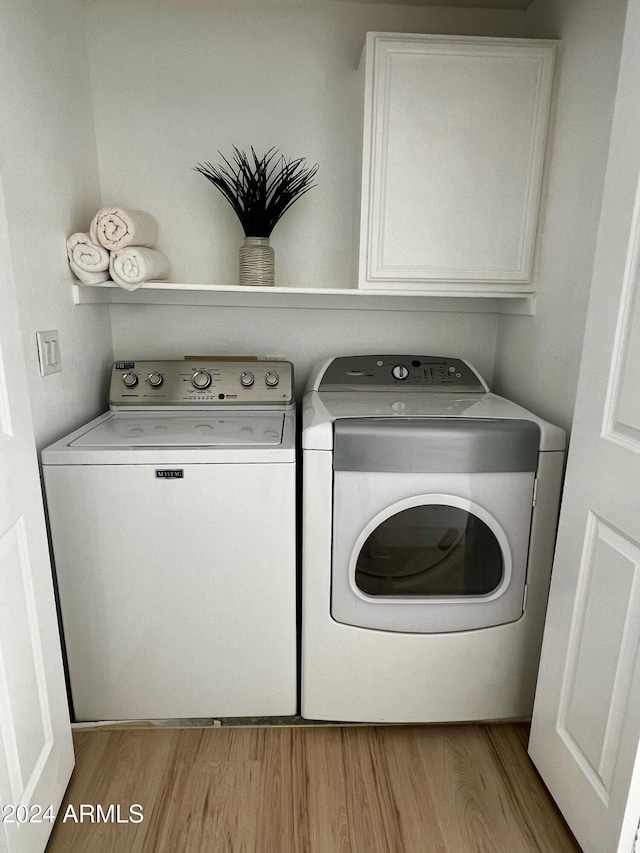 clothes washing area featuring washing machine and clothes dryer, light wood-type flooring, and cabinets