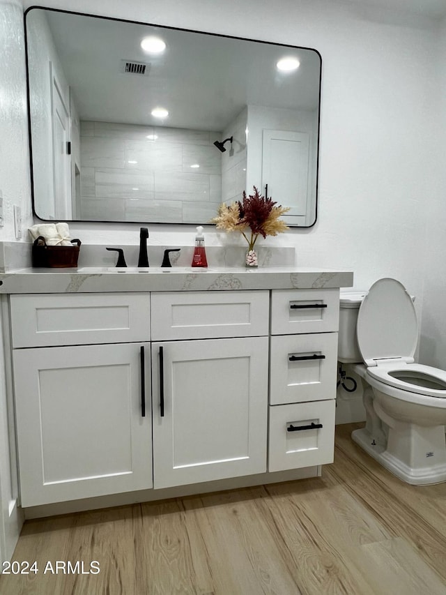 bathroom with vanity, toilet, hardwood / wood-style flooring, and a tile shower