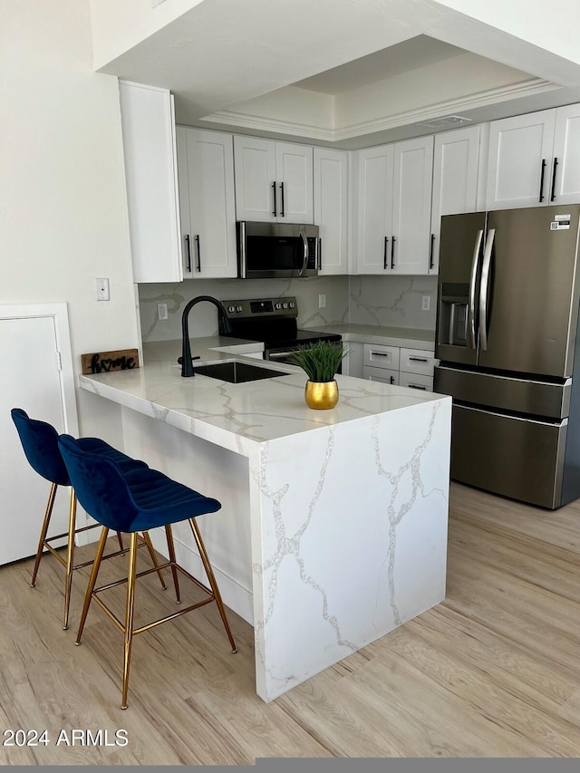 kitchen featuring kitchen peninsula, sink, white cabinets, appliances with stainless steel finishes, and light hardwood / wood-style floors