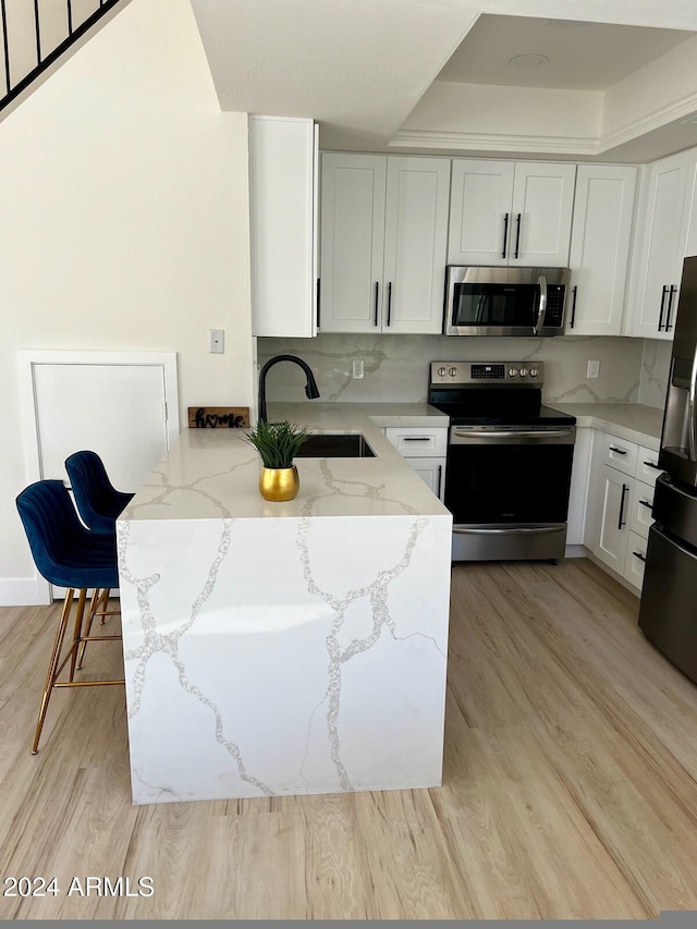 kitchen with light stone counters, white cabinetry, sink, light hardwood / wood-style floors, and stainless steel appliances