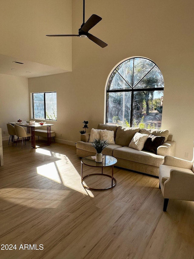 living room featuring a towering ceiling, light hardwood / wood-style flooring, and ceiling fan