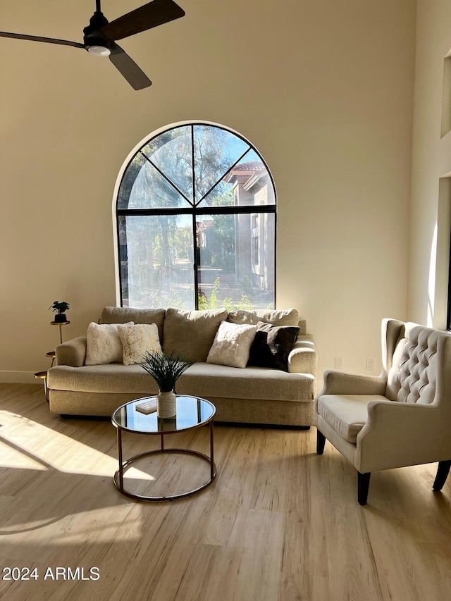 living room featuring a towering ceiling, light wood-type flooring, and ceiling fan