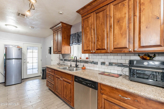 kitchen featuring decorative backsplash, light stone counters, a textured ceiling, sink, and stainless steel appliances